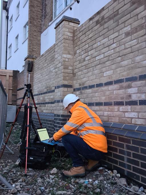A VMS Engineer kneeling down looking on a laptop at noise monitoring data